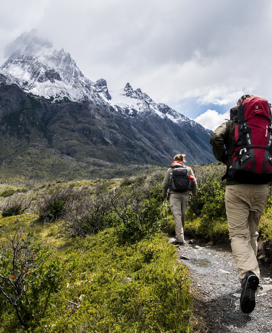 Two hikers with packs on a gravel trail below a glaciated massif